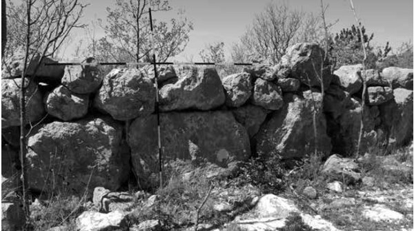 Zid južno od prapovijesnih kuća, na položaju istočno od Tolića kuća u Podbiokovlju, od kojih je odijeljen širokom popločenom ulicom (Igor Hrstić ”O ostatcima megalitskih tvorbi u Tučepima, o toponimu Dračevice i o kultu Peruna i Velesa”), broj 3 iz lipnja 2021.)